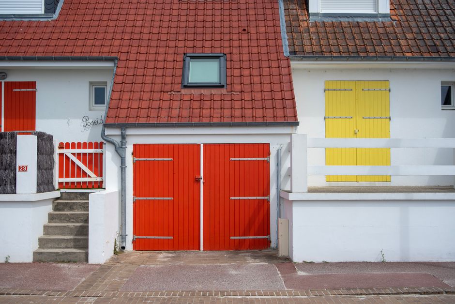 Painted house front with red and yellow doors under a tiled roof.